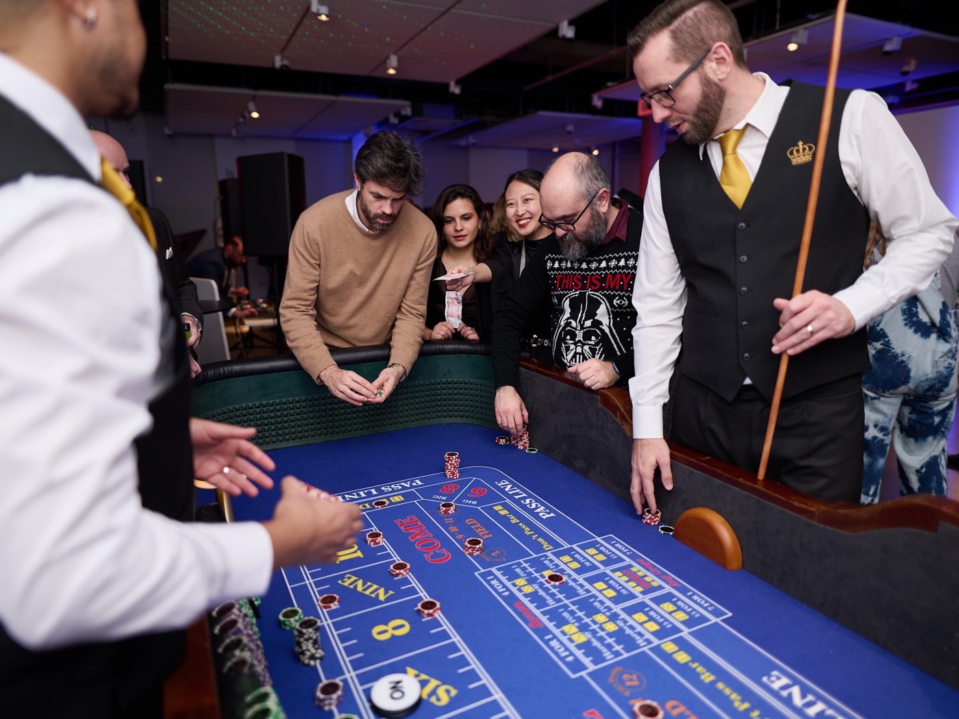 Guests around a Craps table at a Christmas party, with two uniformed croupiers running the game